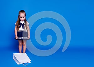 Unhappy little pretty girl, in a dress, looking on the white shopping bag sitting on the floor, over blue background