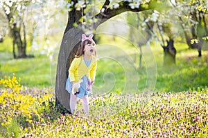 Unhappy little sad and angry crying bunny girl holding rabbit toy in the spring blossom garden