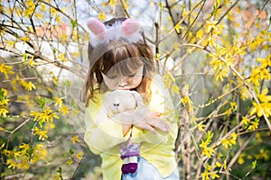 Unhappy little sad bunny girl holding rabbit toy in the spring blossom garden