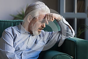 Unhappy lonely grey haired mature man sitting on couch