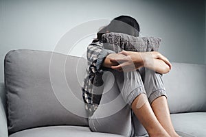 Unhappy lonely sad woman is sitting on the couch and hiding her face on a pillow, depression concept