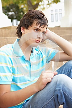 Unhappy Male Teenage Student Sitting Outside