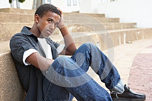 Unhappy Male Teenage Student Sitting Outside