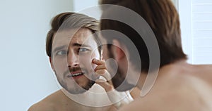 Unhappy man looking in mirror worried about facial skin problem