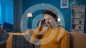 Unhappy man sitting on the sofa in the living room suffers from a headache close up. A person feels bad from tension