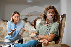 Unhappy married couple arguing among themselves while sitting on a Victorian sofa at home