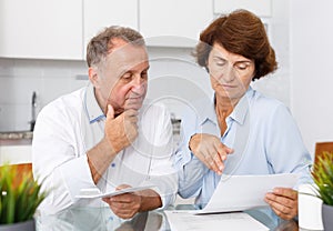 Unhappy mature family couple sitting at kitchen table with documents