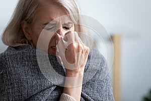 Unhappy mature woman covered blanket feeling bad, sneezing