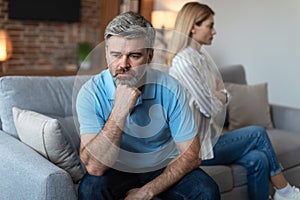 Unhappy middle aged european man ignores offended lady after quarrel in living room interior