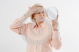 Unhappy Middle aged Woman looking in mirror on her face with wrinkles on the forehead and wrinkle skin. Collagen and face