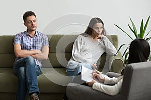 Unhappy millennial couple sitting apart on couch visiting female