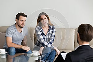 Unhappy millennial couple talking to psychologist sitting on couch