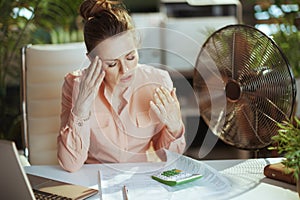 unhappy modern female worker at work with electric fan