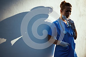 Unhappy modern physician woman outdoors in city near wall