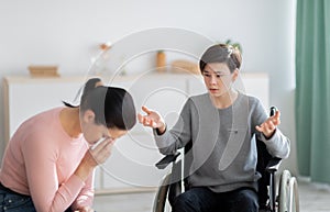 Unhappy mother crying and her disabled teen son in wheelchair trying to justify himself after disagreement at home photo