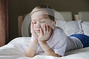 Unhappy offended little boy sitting alone on the bed. Loneliness, naughtiness concept