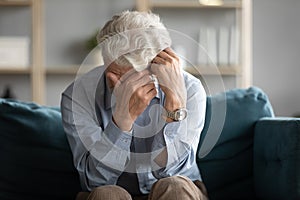 Unhappy old man sit on couch crying yearning