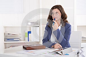 Unhappy older pensive business woman sitting at desk.