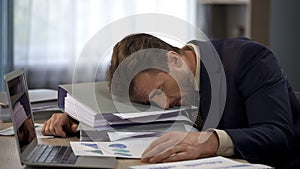 Unhappy overworked male manager lying on pile of folders at workplace, tiredness photo