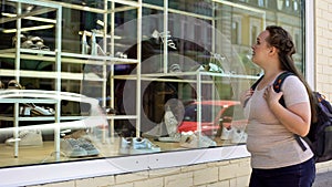 Unhappy poor female looking at shop window with shoes, expensive footwear