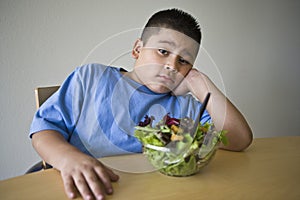 Unhappy preadolescent Boy Sitting At Desk With Salad