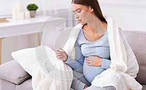 Unhappy Pregnant Lady Measuring Temperature Sitting On Couch At Home