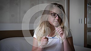 Unhappy pregnant woman, worried girl looks at pregnancy test sitting on edge of the bed in room