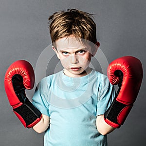 Unhappy preschooler with red hair showing his boxing gloves