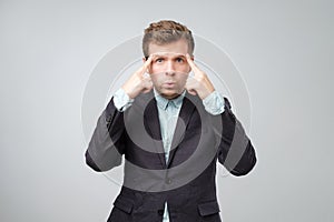 Unhappy puzzled young man pointing at his head with fingers and looking at camera.