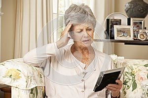 Unhappy Retired Senior Woman Sitting On Sofa At Home Looking At Photograph