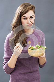 Unhappy 20s girl questioning the taste of a mixed green salad