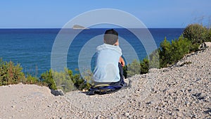 Unhappy sad boy sitting alone hugging his knees outdoors near the sea. Child depression, abuse, children problems