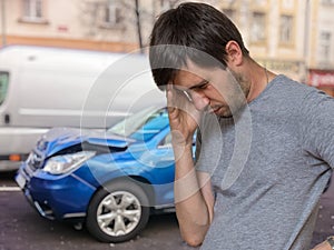Unhappy sad driver had car accident. Destroyed car in background