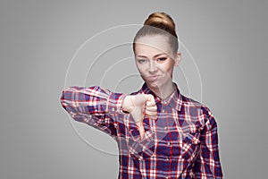 Unhappy sad girl with pink checkered shirt, collected bun hairstyle and makeup standing and looking at camera with unsatisfied fa