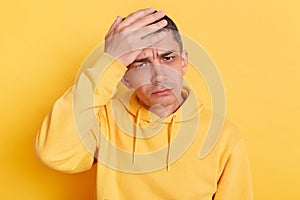 Unhappy sad man wearing casual style hoodie, posing isolated over yellow background, making facepalm gesture, loser, forget about