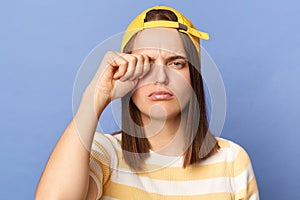 Unhappy sad upset teenager girl wearing striped t-shirt and baseball cap standing isolated over blue background feeling fatigue