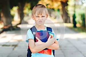 Unhappy school boy with books in hands and backpack. Sad schoolboy with negative emotions go to school