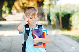 Unhappy school boy with books in hands and backpack. Upset kid going to school