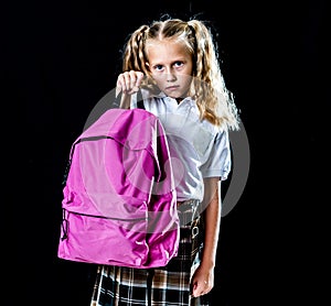 Unhappy school girl holding a big schoolbag full of books and homework isolated on black background in back to school learning