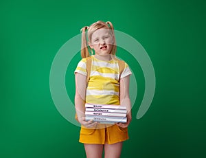 Unhappy school girl with schoolbooks on green background