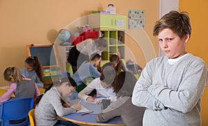 Unhappy schoolboy standing at class, children drawing