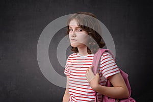 Unhappy schoolgirl holding backpack, looking at camera