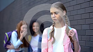 Unhappy schoolgirl standing front of laughing cruel pupils, college mocking