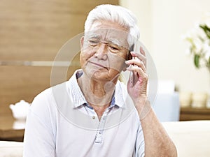 Unhappy senior asian man talking on phone