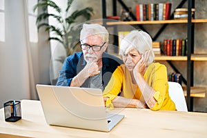 Unhappy senior couple looks at laptop screen