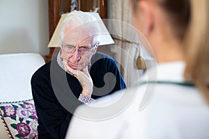 Unhappy Senior Man Being Visited By Female Nurse