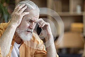 Unhappy senior man having phone conversation, home interior