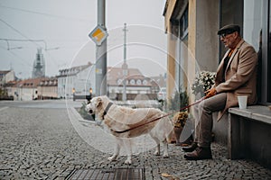 Unhappy senior man sitting on bench in front of store and waiting somebody wih his big white dog.