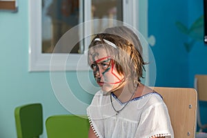 Unhappy serious, angry little girl with painted face sitting inside the room