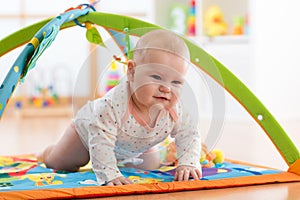 Unhappy seven months baby girl crawling on colorful playmat photo